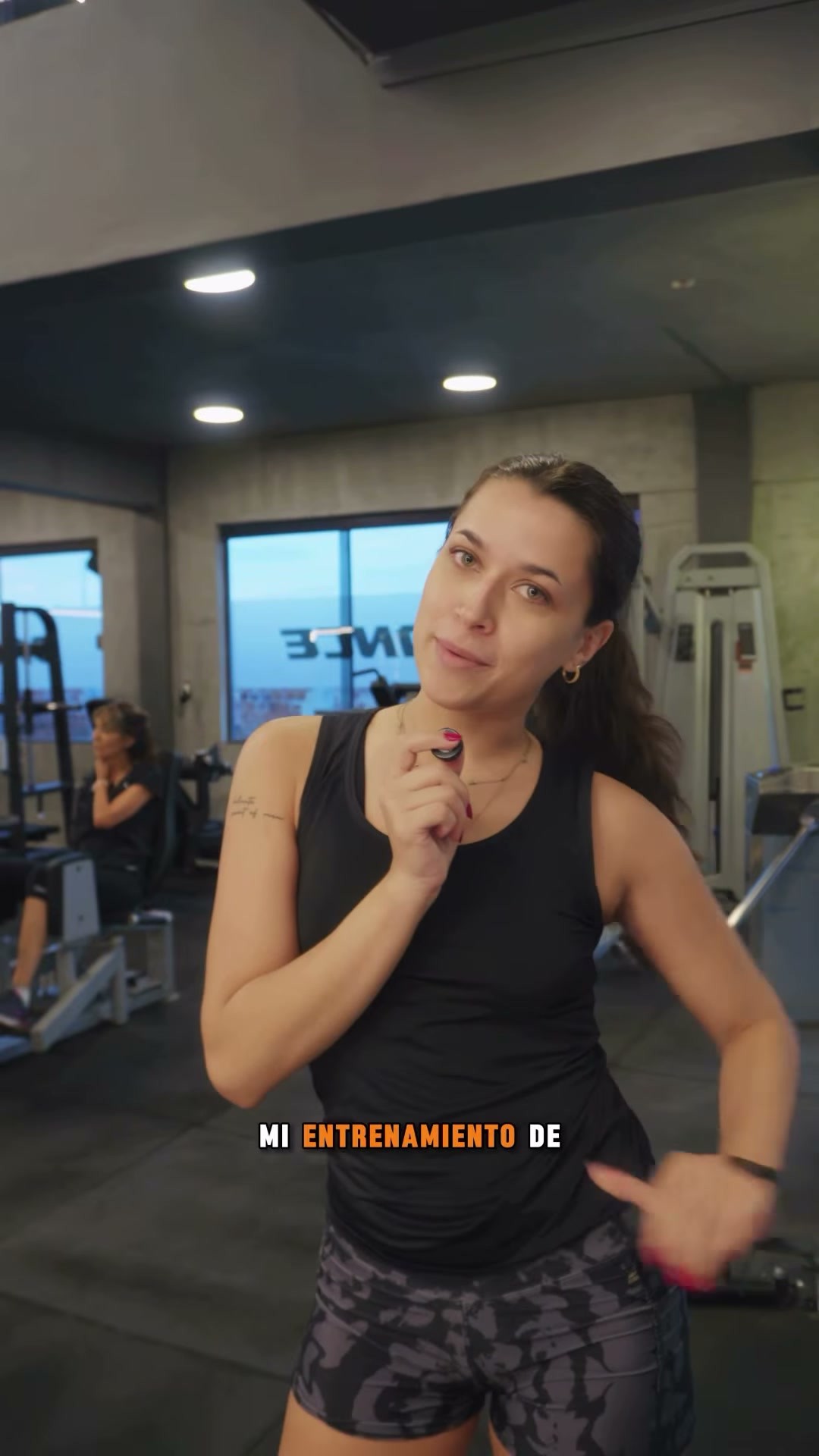 Aldi con top negro y shorts oscuros, sosteniendo un micrófono en Balance Fitness